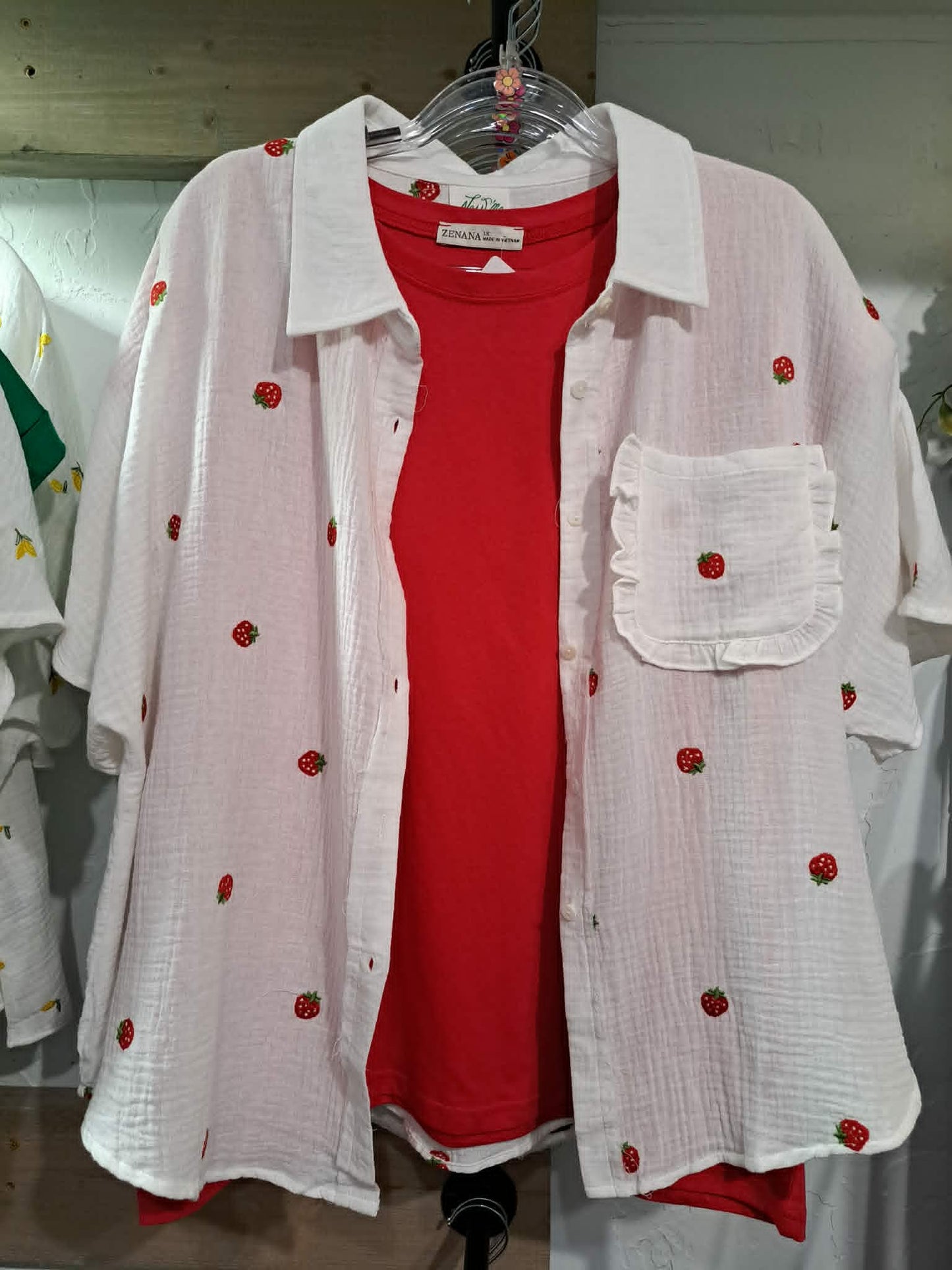 White shirt with red floral embroidery on a hanger against a white background