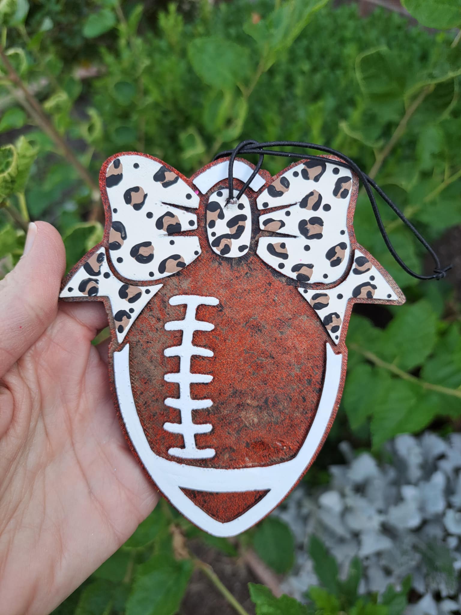 Decorative football air freshener with leopard bow held against a foilage background