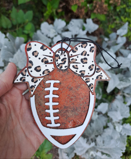 Decorative football freshie with leopard print bow held against a natural background