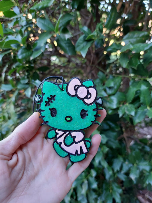 hand holding frankenstein kitty air freshener in front of foilage