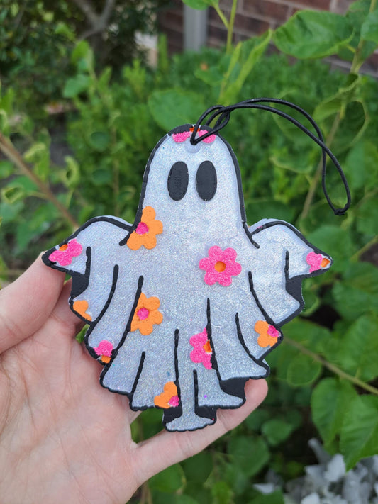 Decorative ghost freshie with flowers held in a hand against a green leafy background