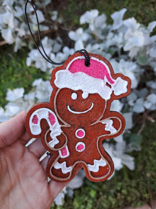 Decorative gingerbread man freshie with a pink hat held against a blurred natural background.
