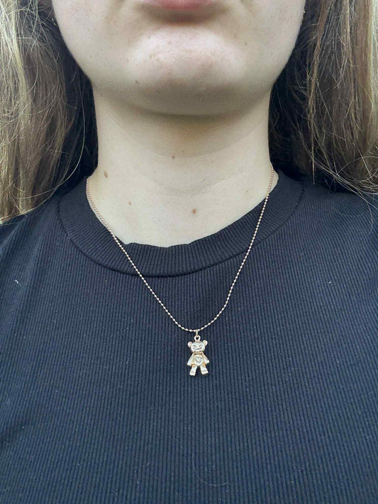 Person wearing a black shirt with a necklace featuring a small bear pendant.