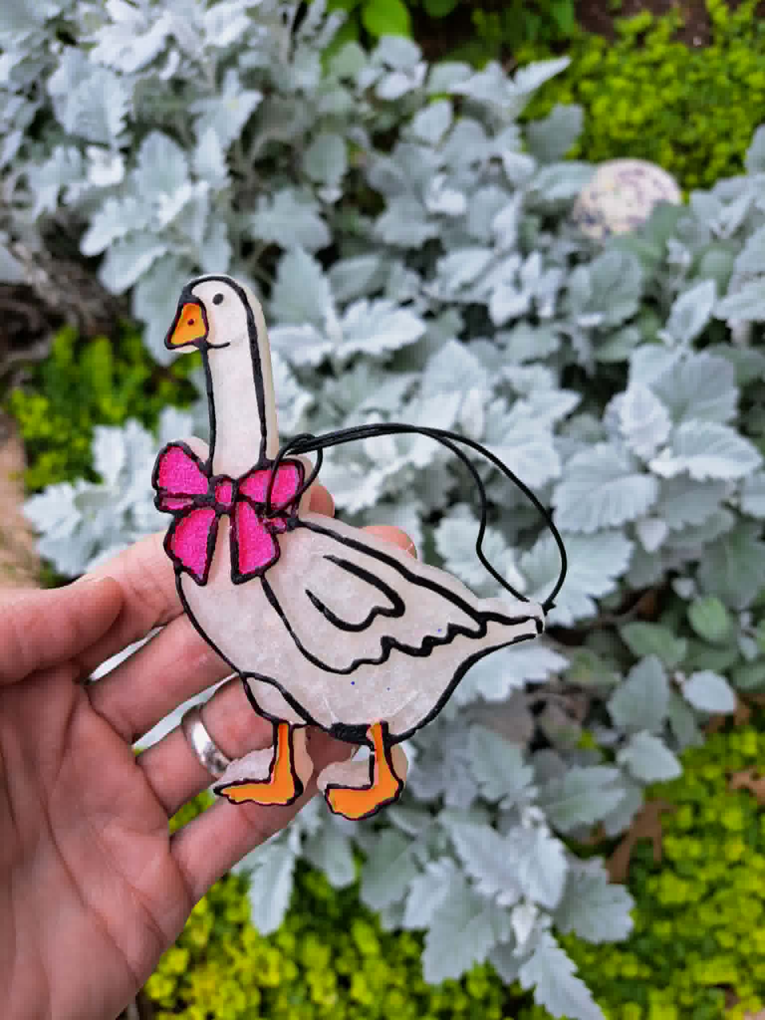 goose freshie with pink bow held in front of leafy background