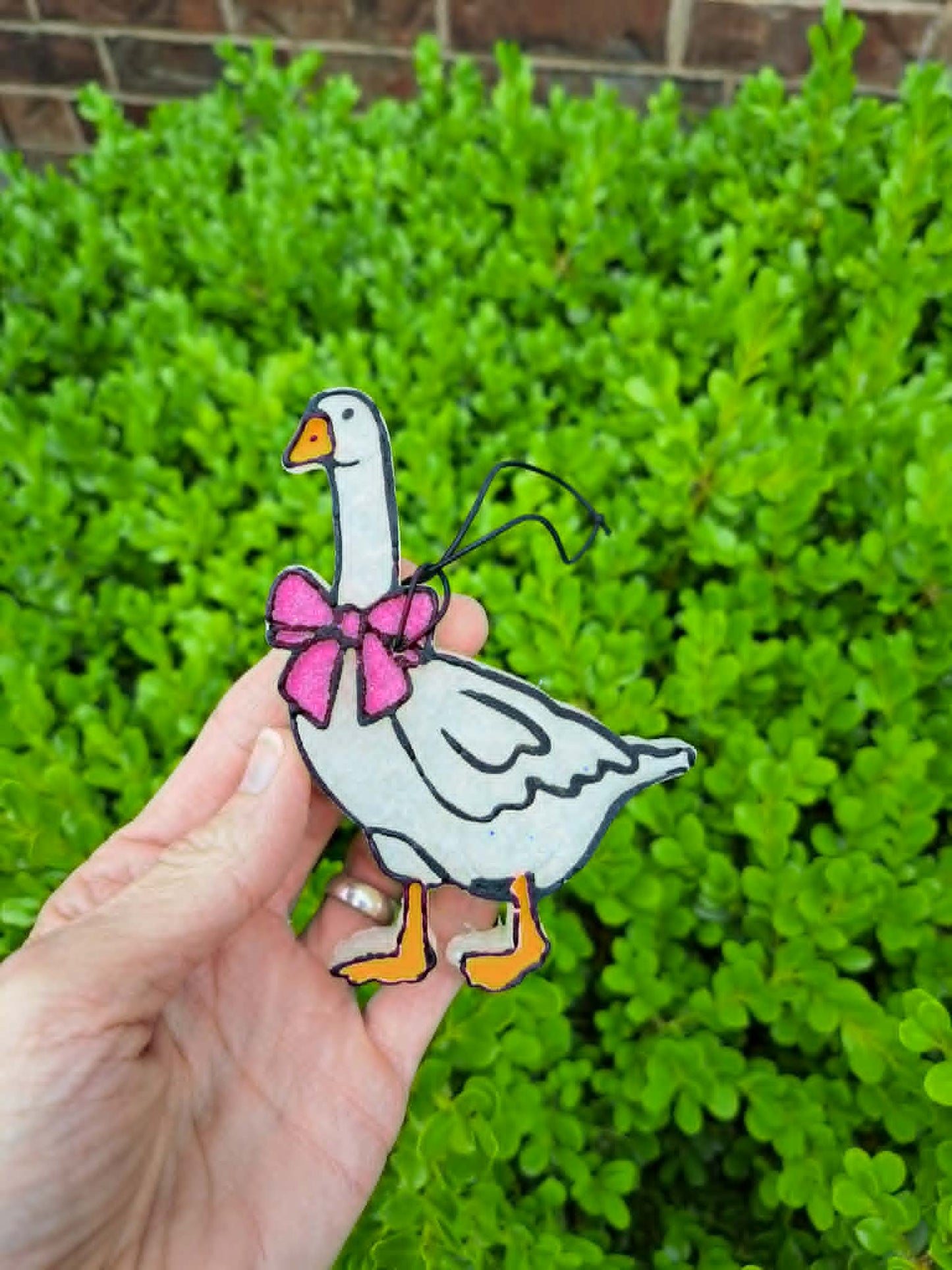 goose freshie with pink bow held in front of leafy background