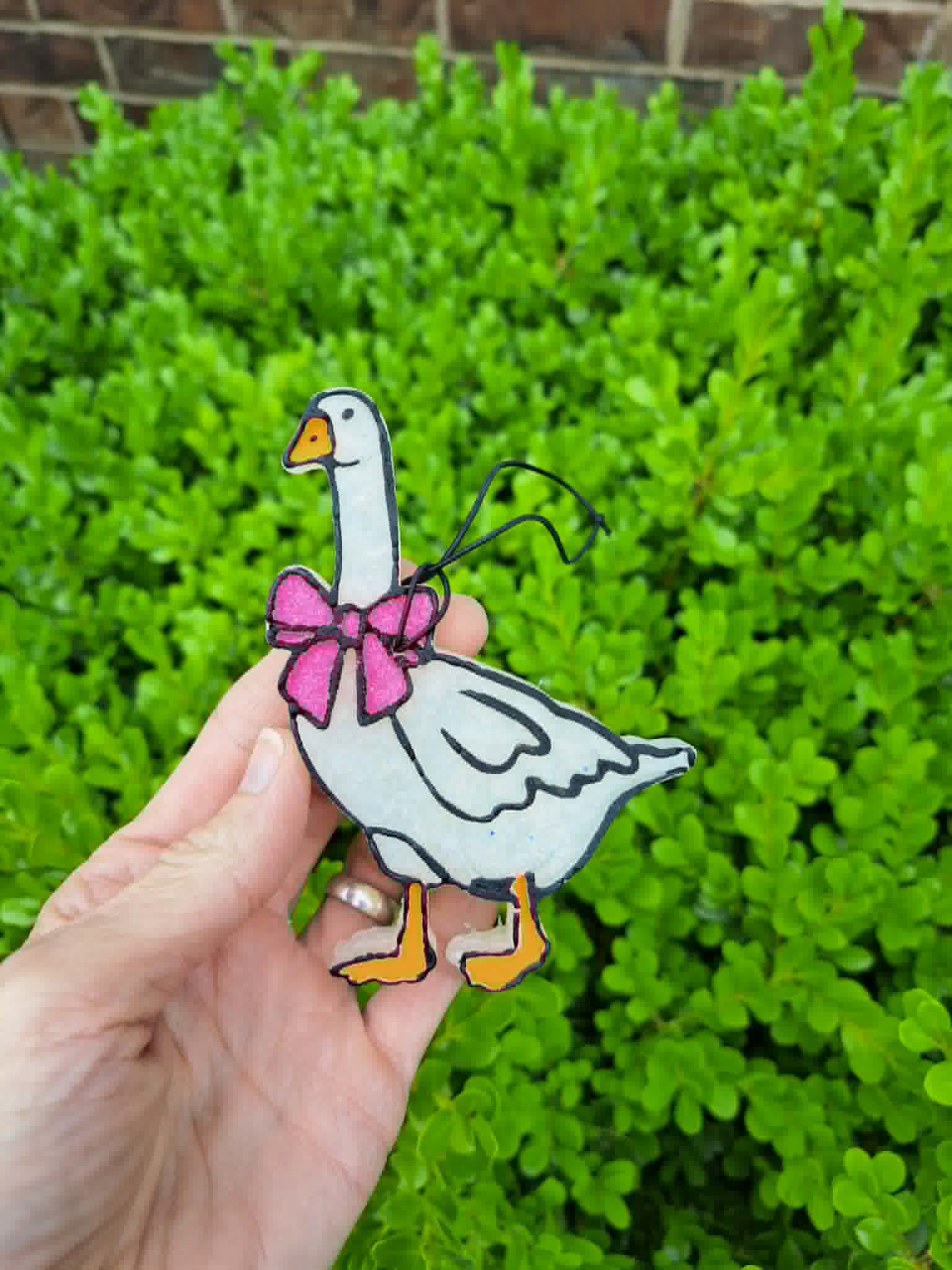 goose freshie with pink bow held in front of leafy background