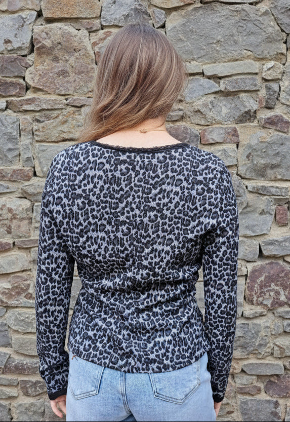 Person wearing a leopard print top and light blue jeans standing in front of a stone wall