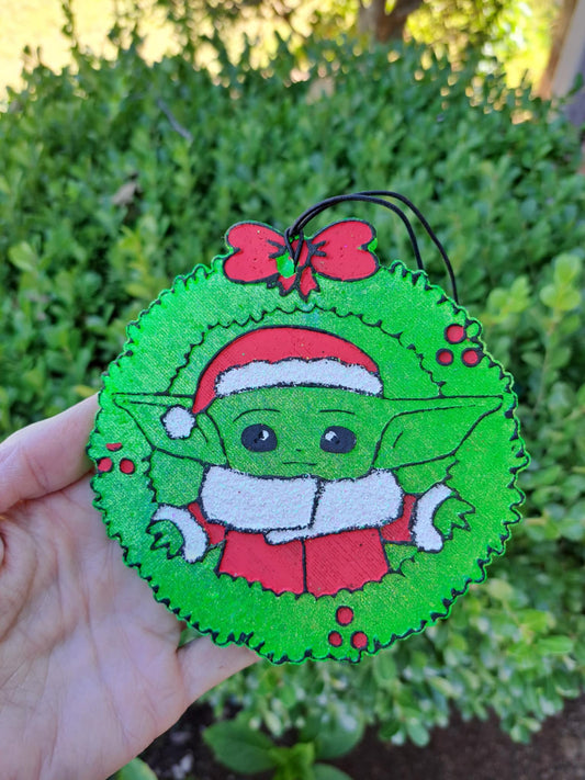Freshie with a character in a Santa hat held in front of green foliage.
