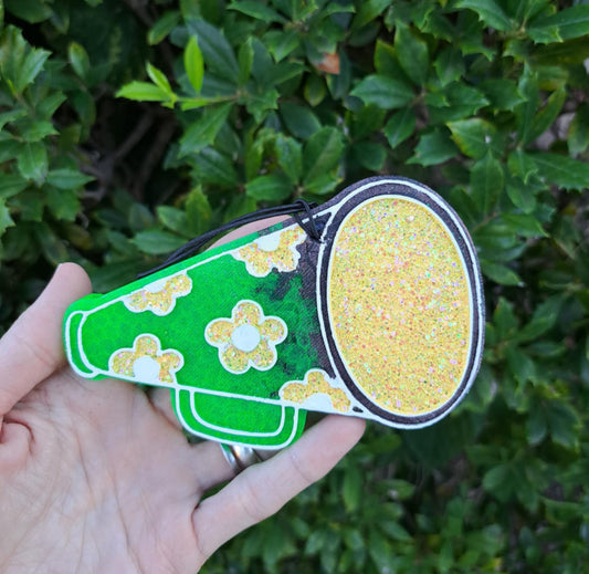 Hand holding a green and yellow megaphone with floral patterns against a green leafy background.