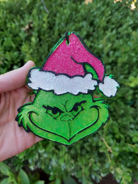 Green grinch with pink glittery santa hat held against a green leafy background