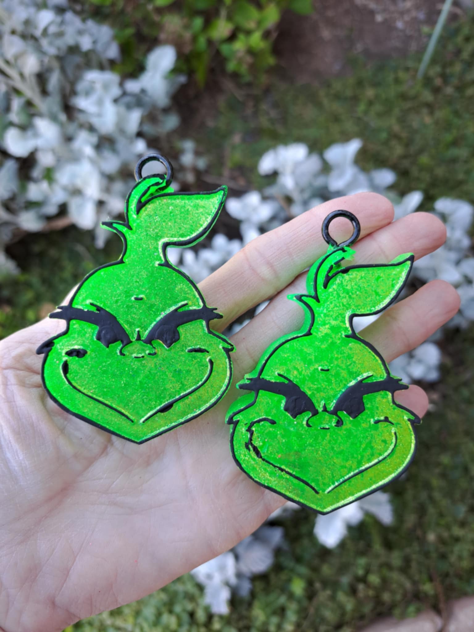 Green Grinch face vent clips held in a hand with a blurred natural background