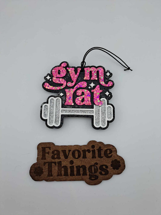 A handmade, silver and pink air freshener with the text 'Gym Rat' and a barbell symbol on top, and a brown tag reading 'Favorite Things' at the bottom.
