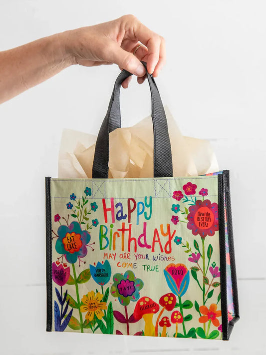 Hand holding a colorful gift bag with floral design and 'Happy Birthday' text.