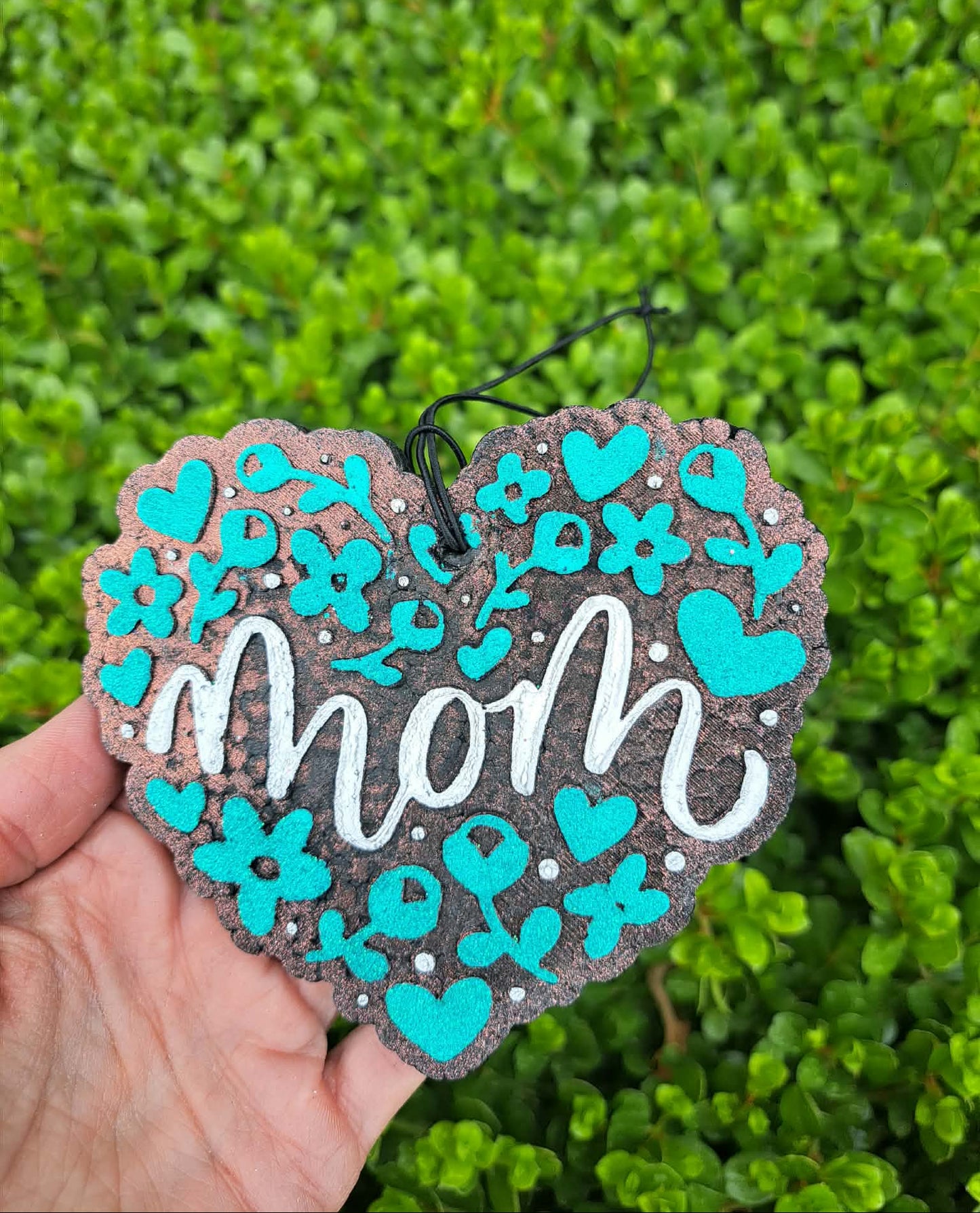 Heart-shaped decorative freshie with 'mom' text and turquoise flowers against a green leafy background