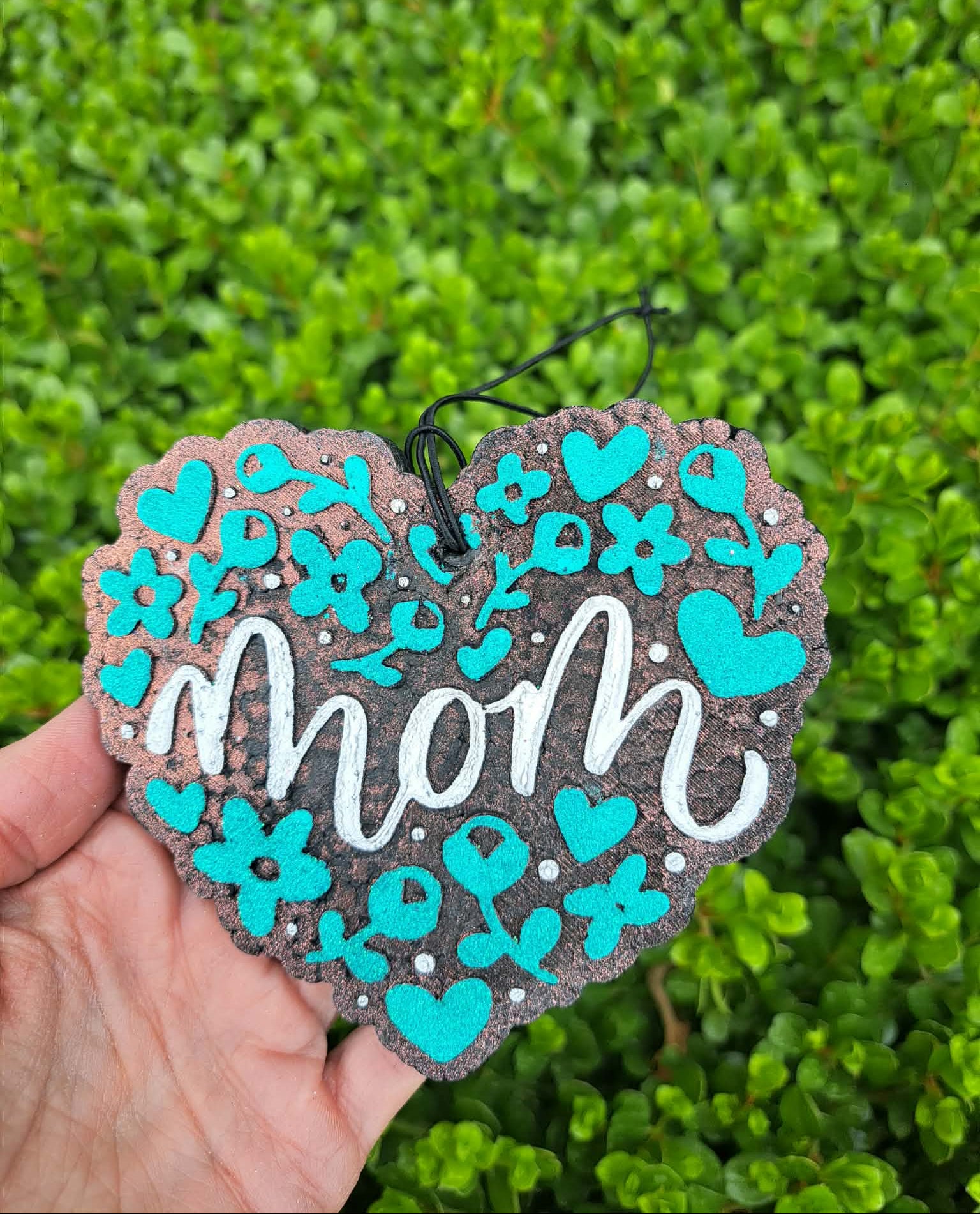Heart-shaped decorative freshie with 'mom' text and turquoise flowers against a green leafy background