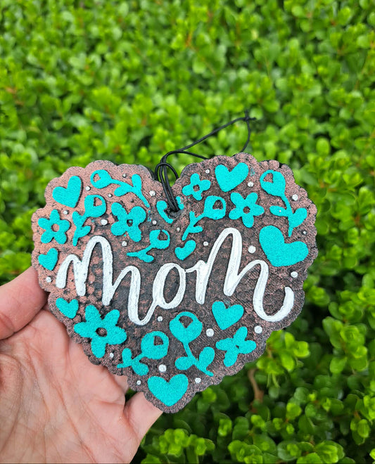 Heart-shaped decorative freshie with 'mom' text and turquoise flowers against a green leafy background