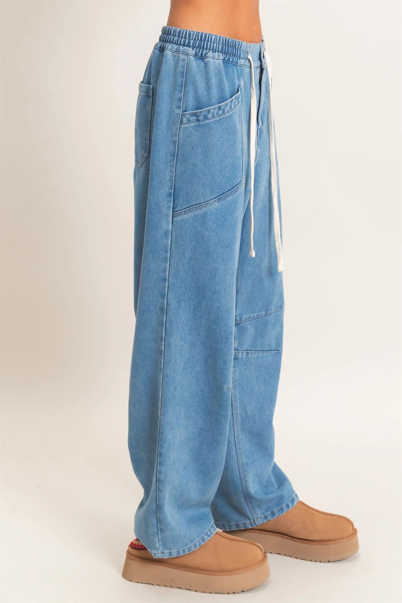 A person wearing wide-leg light blue denim pants with an elastic drawstring waist and tan platform slippers, shown from the waist down against a plain light background.