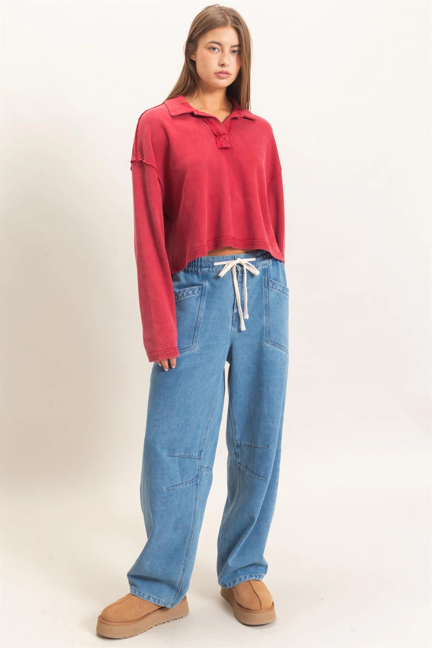 Woman wearing a red long-sleeve top and blue jeans on a white background