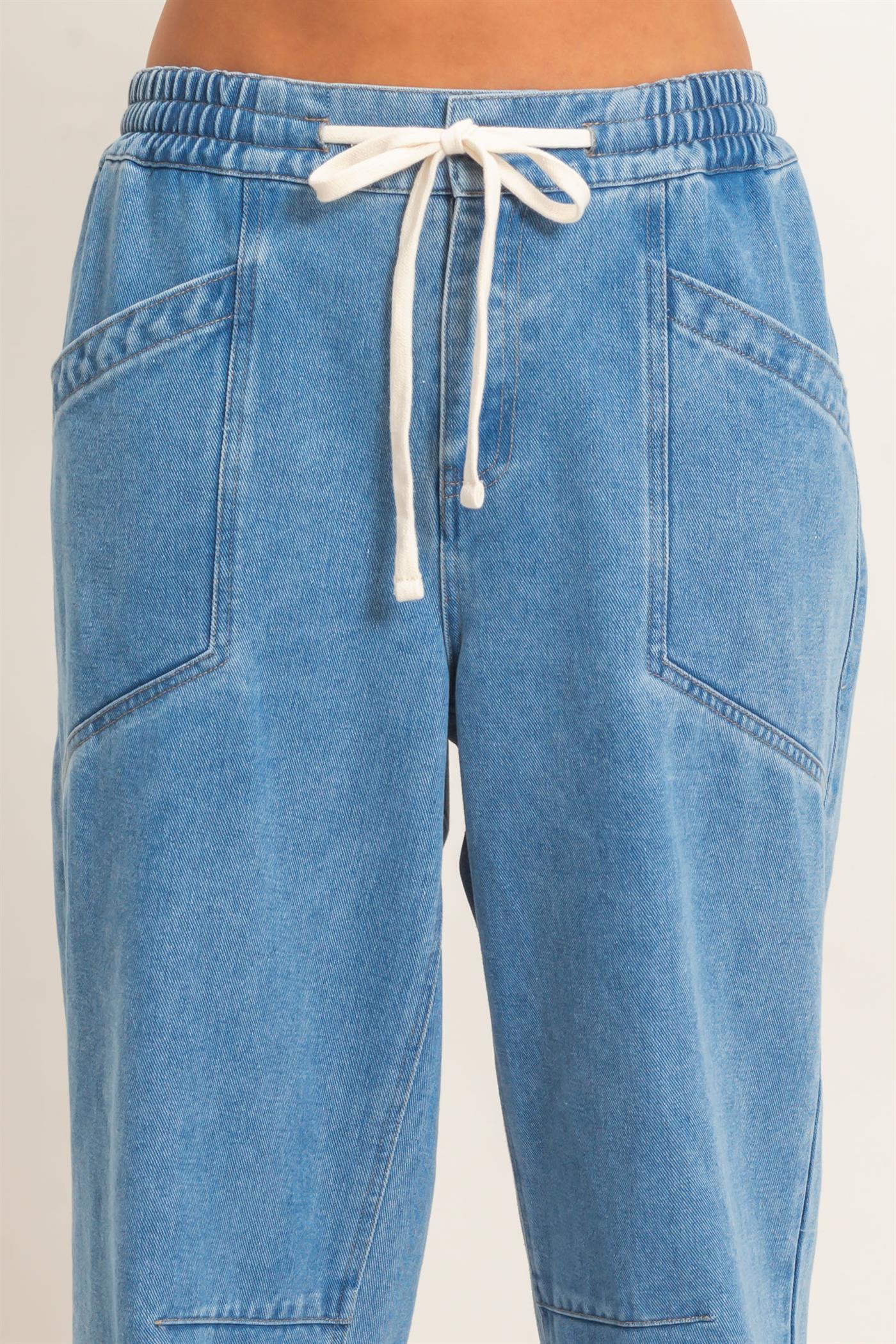 Blue denim jogger pants with a white drawstring on a beige background