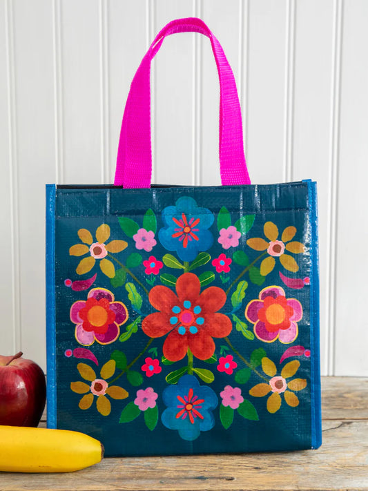 Colorful floral-patterned tote bag with pink handles on a wooden surface.