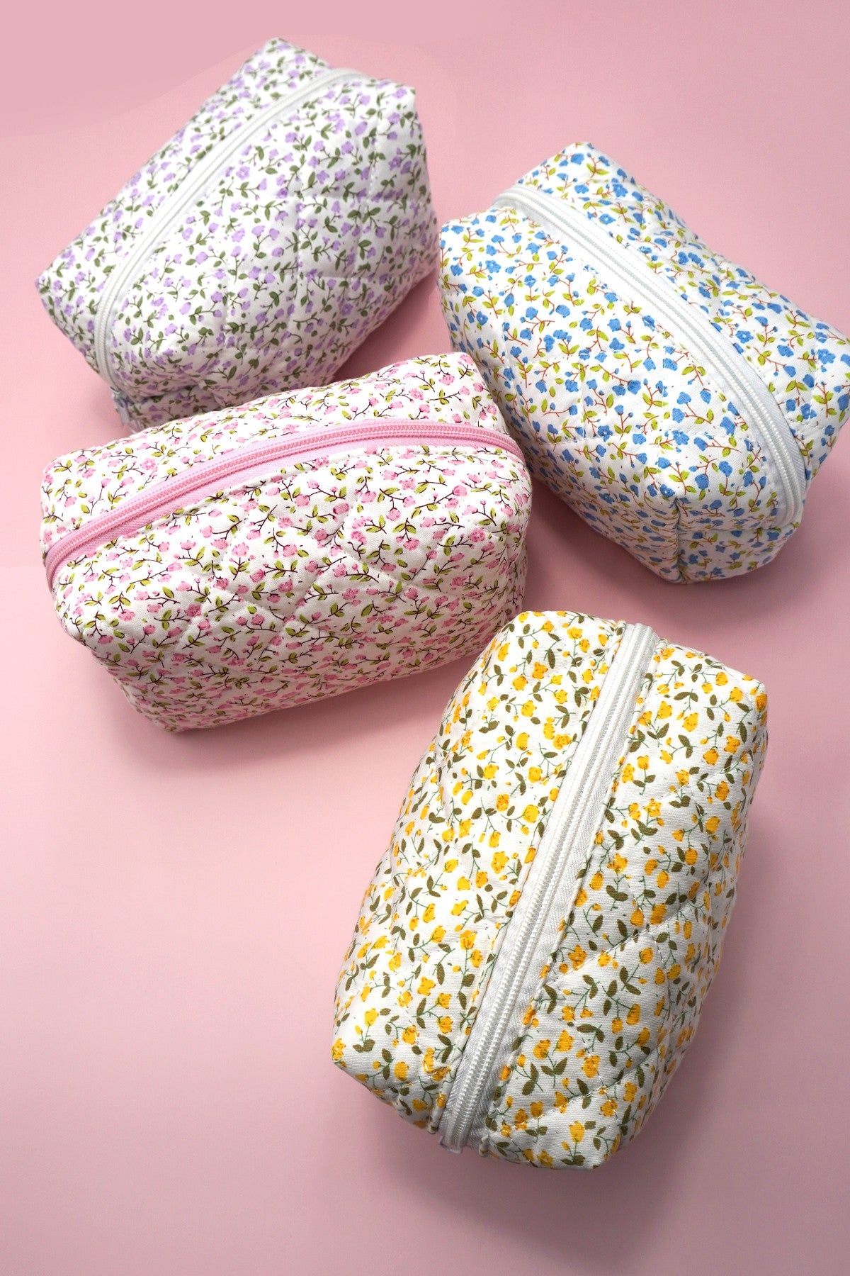 Four floral-patterned pouches with zippers on a pink background