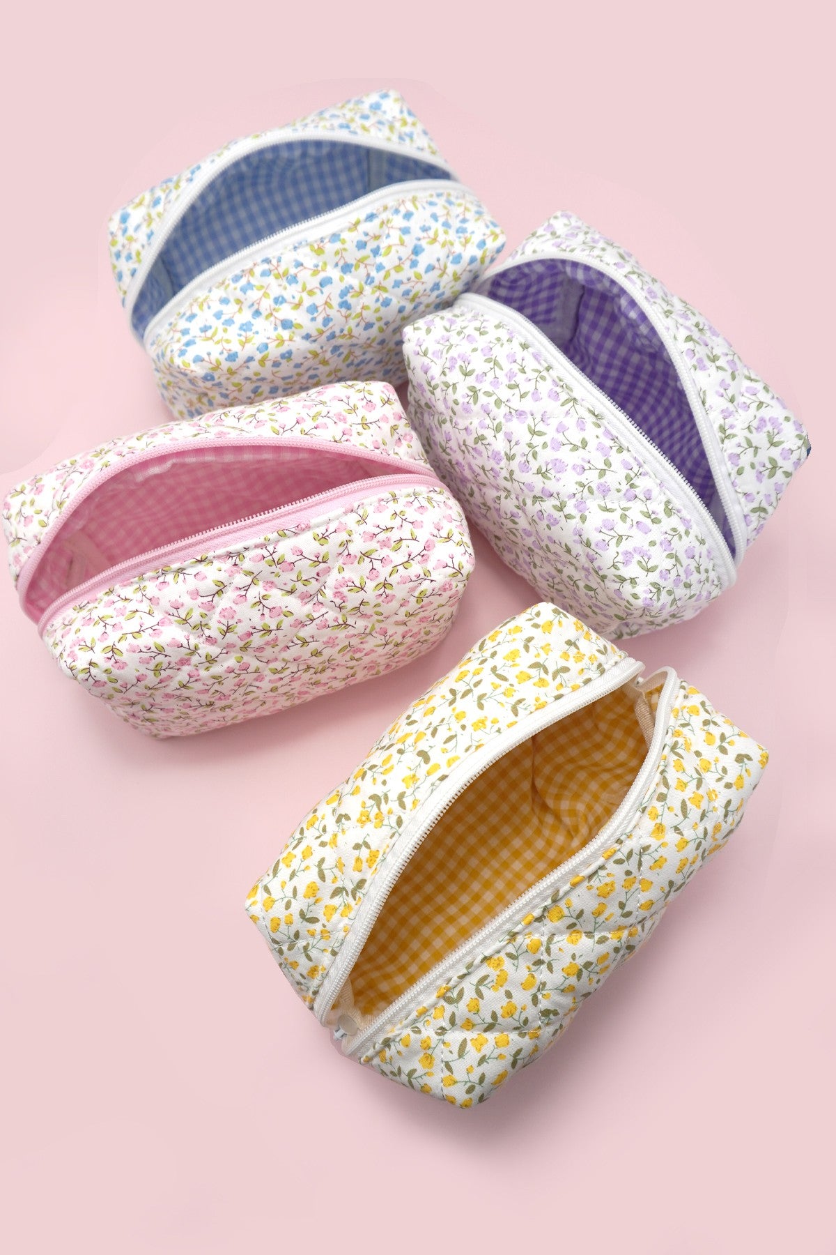 Four small flower print quilted cotton cosmetic bags on a pink background