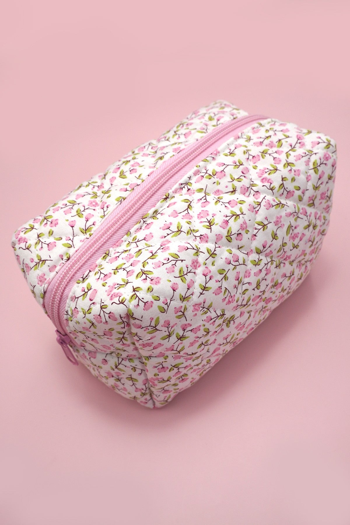 Pink floral-patterned toiletry bag with pink zipper on a pink background