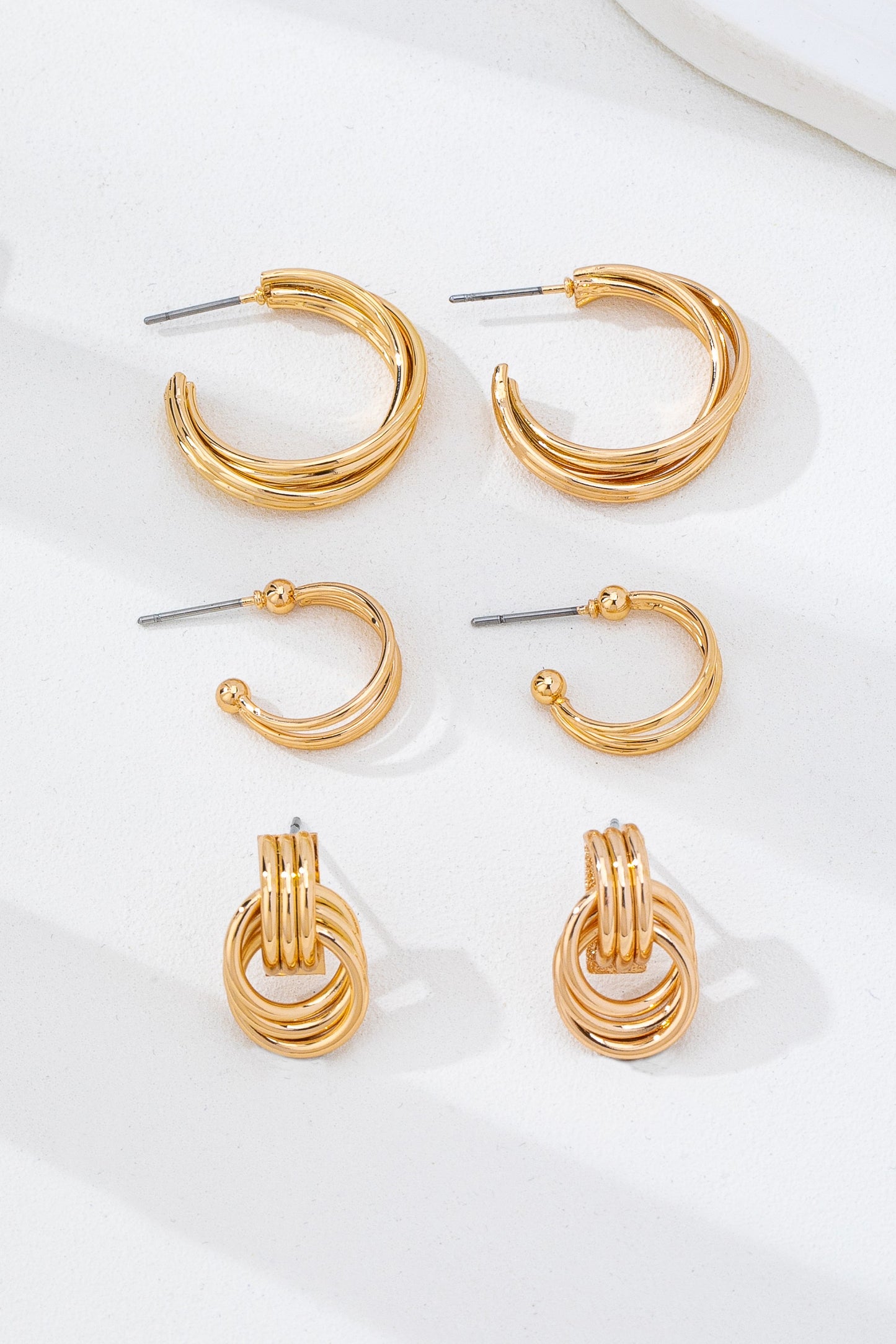 three pairs of gold hoop earrings on a white background