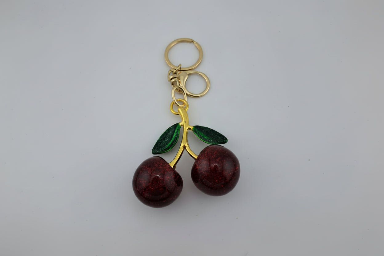 Cherry-shaped keychain with gold stem on a white background