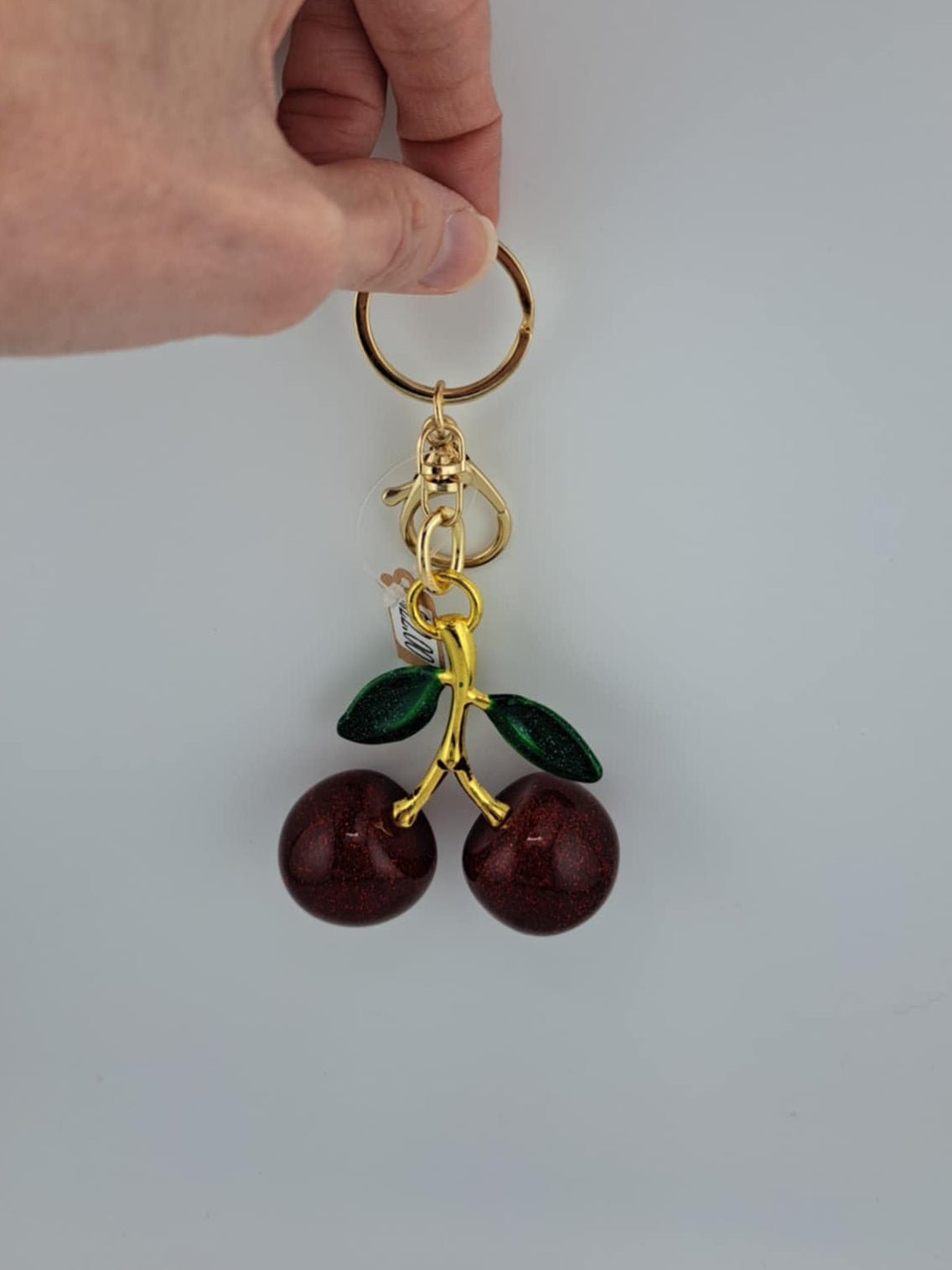 Hand holding a keychain with cherry charm against a white background