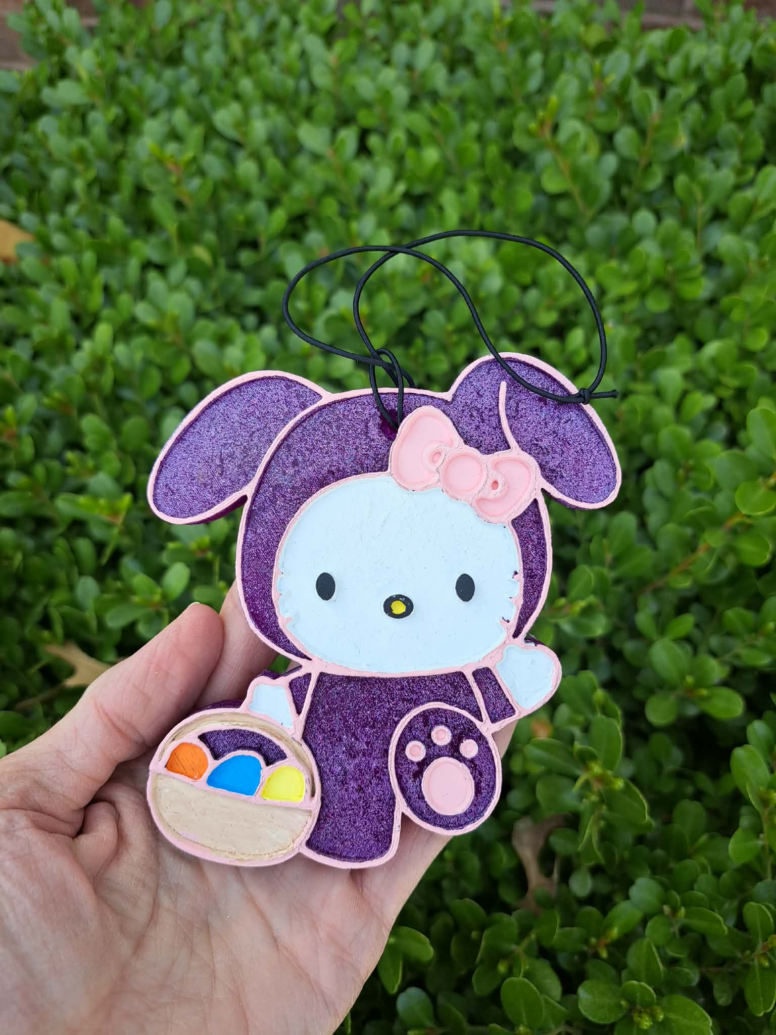 kitty air freshener in a bunny costume held against a green leafy background.