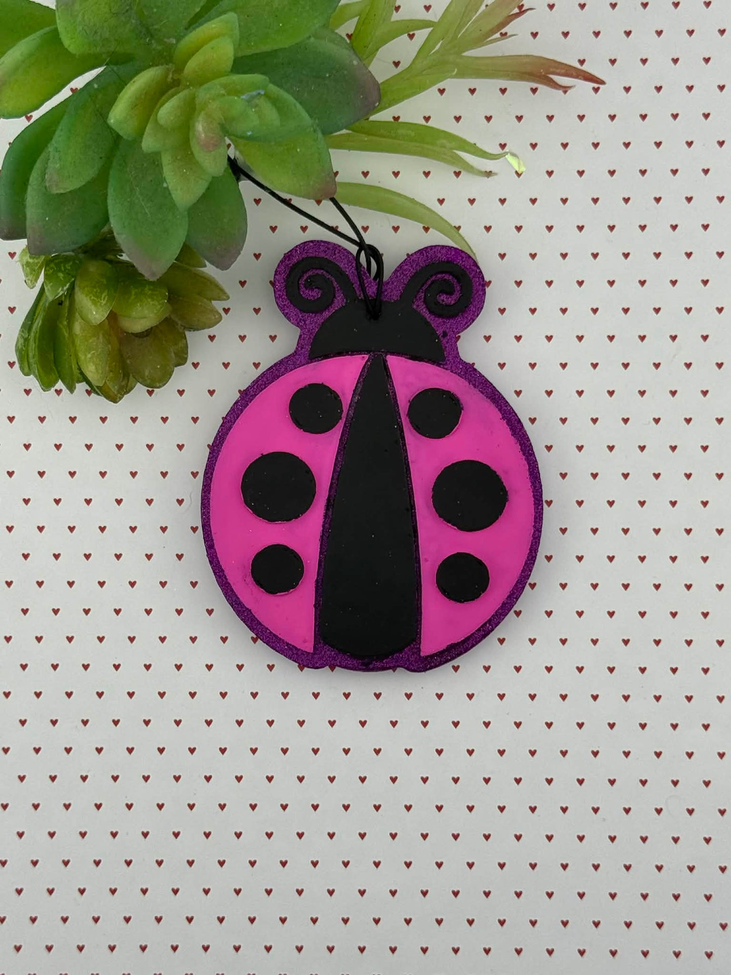 Pink and black ladybug freshie on a white background with green leaves.