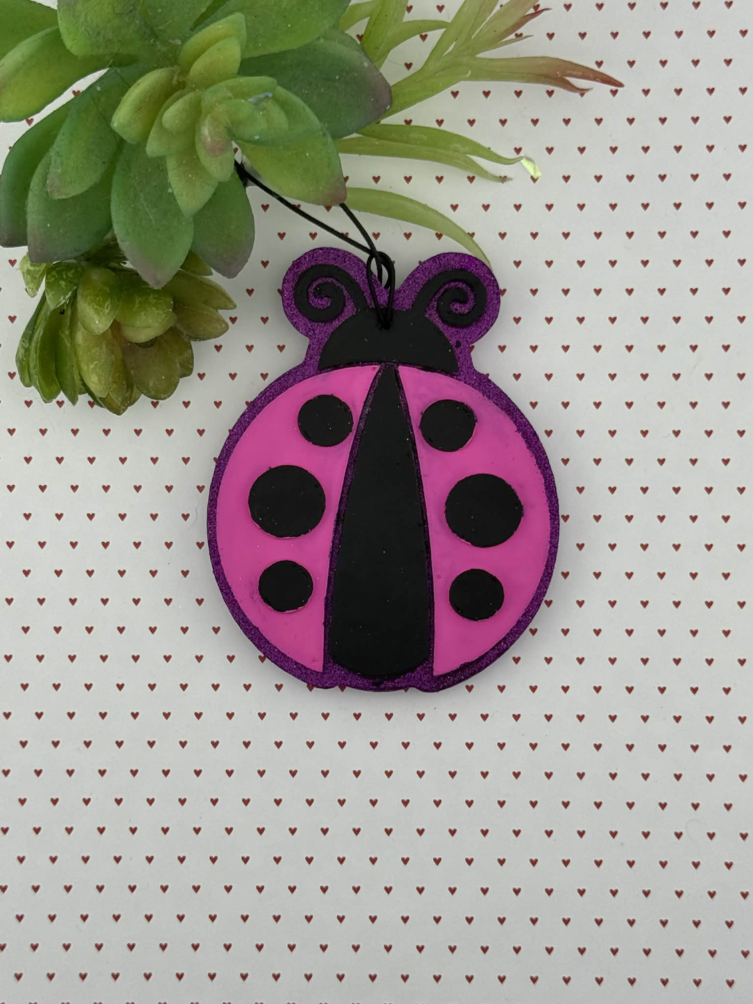 Pink and black ladybug freshie on a white background with green leaves.