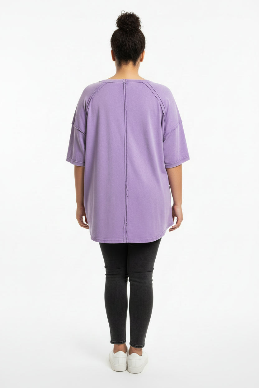 A lavender purple short-sleeve top with a central seam and raglan-style shoulder seams, on a woman with a white background