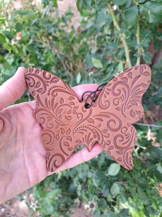 Butterfly-shaped tooled leather freshie held against a blurred green background