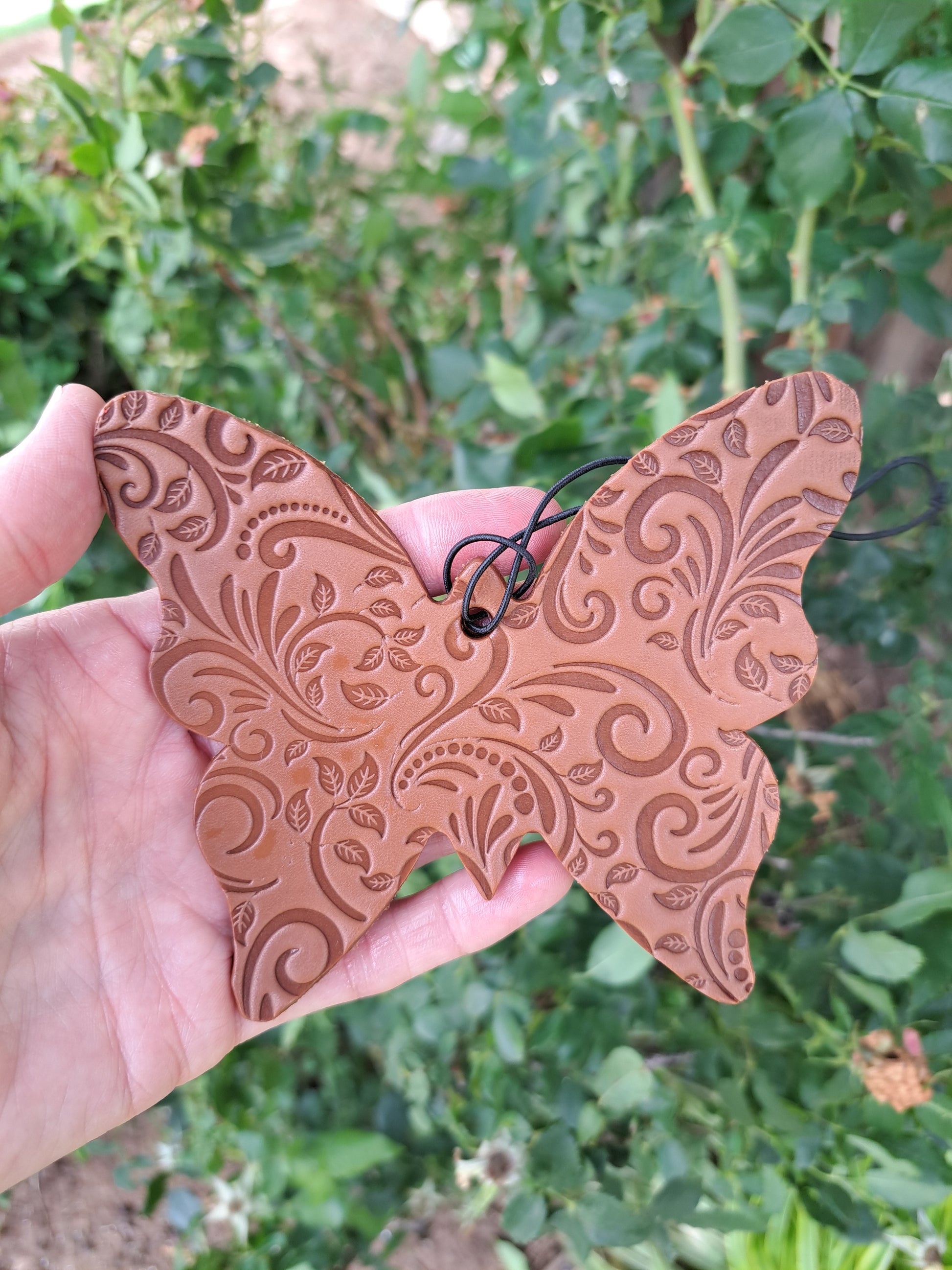 Butterfly-shaped tooled leather freshie held against a blurred green 