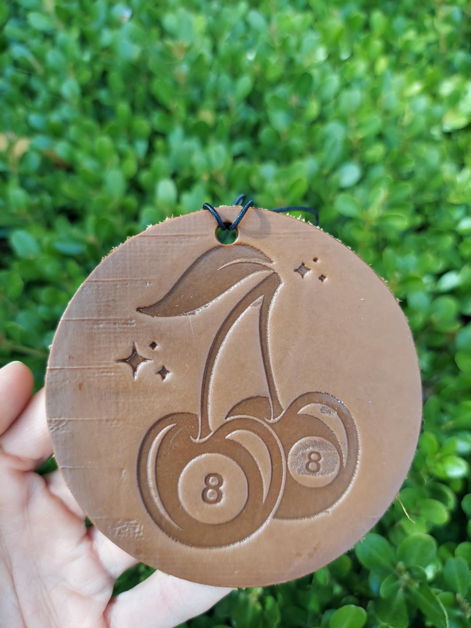 leather cherry round freshie held against a green leafy background