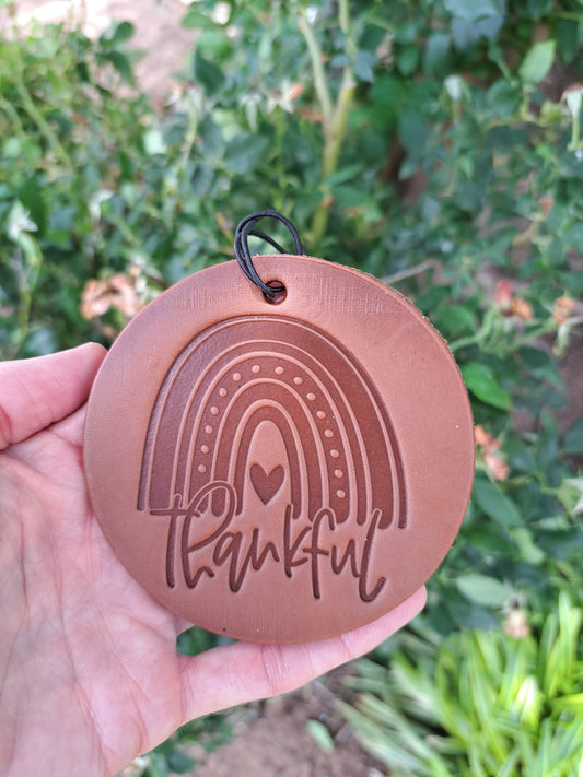 round leather rainbow 'thankful' freshie held in front of greenery
