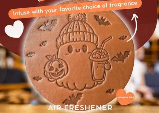 A leather air freshener depicting a cute, cartoon-style ghost wearing a hat and holding a beverage, with autumn-themed decorations around it.