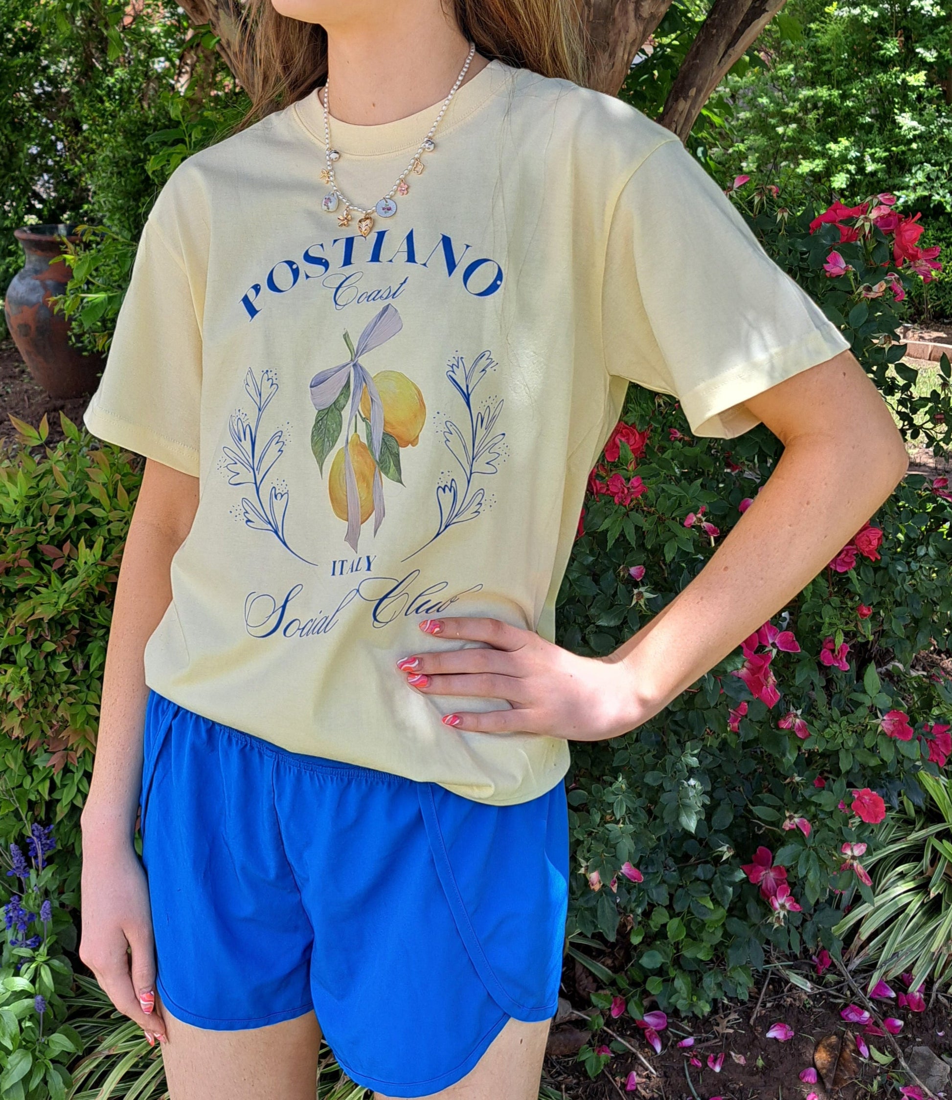 Person wearing a light-colored t-shirt with graphics and text, standing in a garden setting.