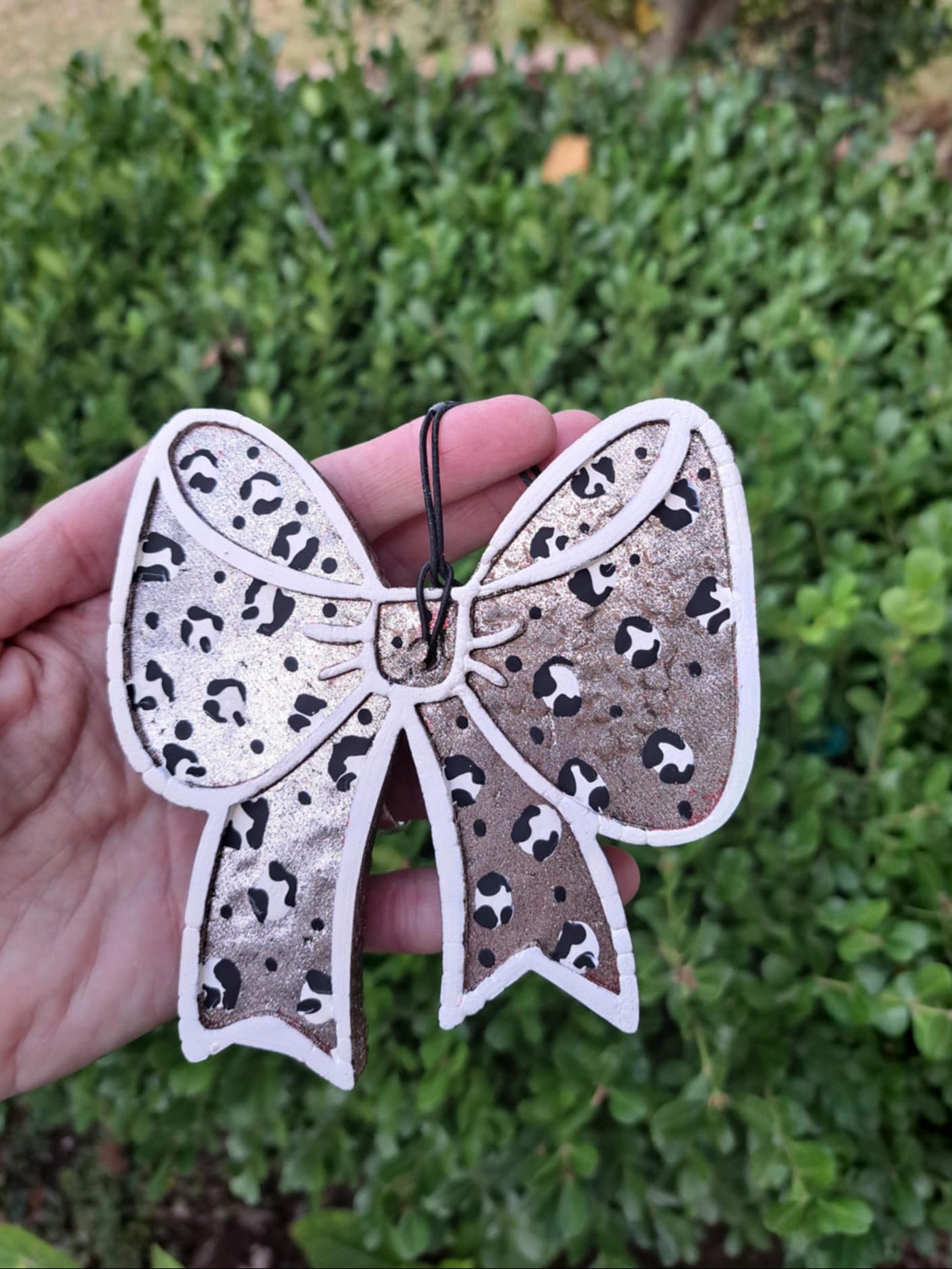 leopard bow freshie held in hand in front of green background