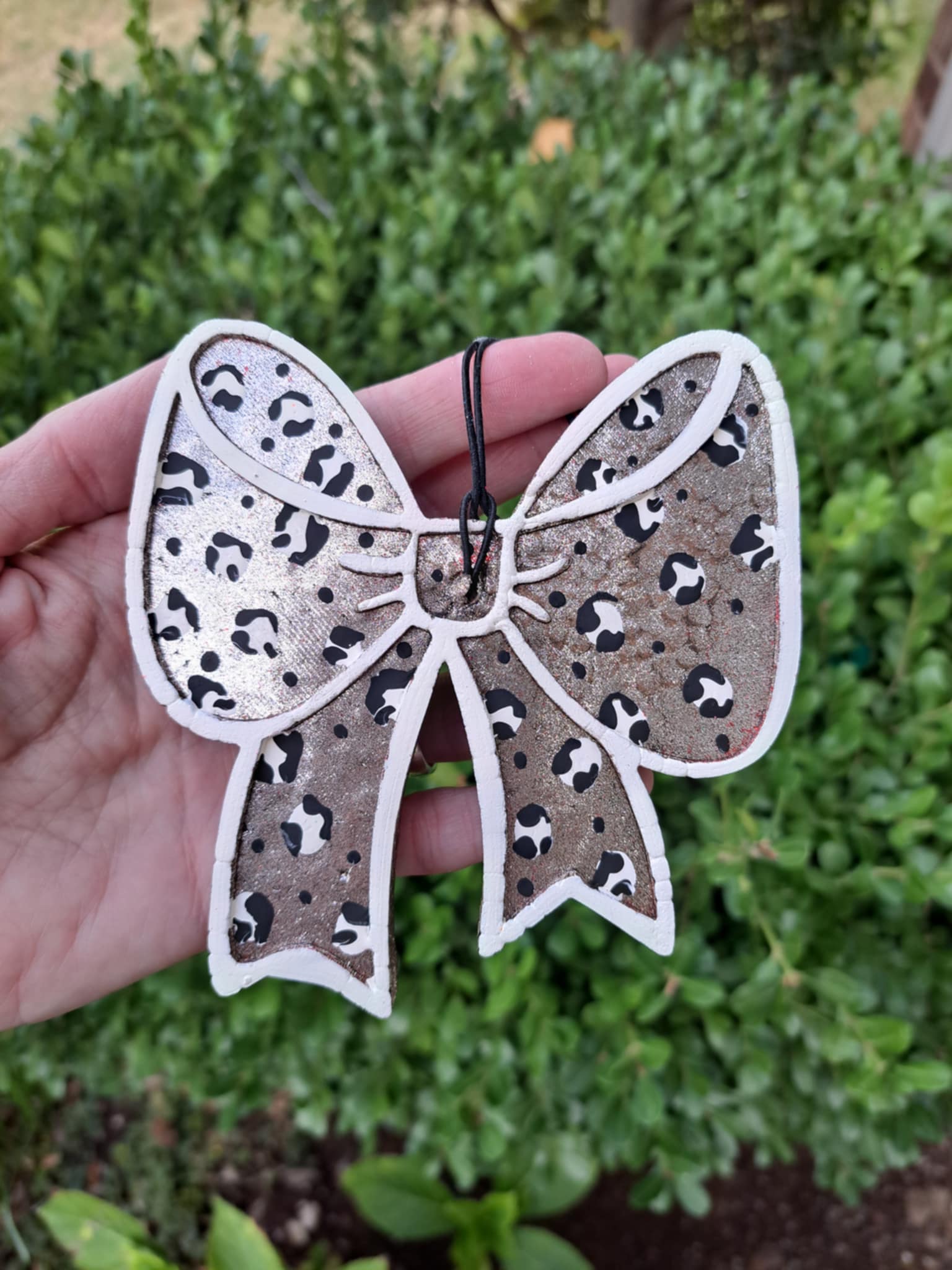 Leopard print bow-shaped freshie held in a hand with a green outdoor background