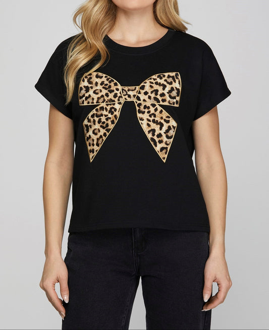 A woman wearing a black top with a leopard print bow on the front, paired with black pants.