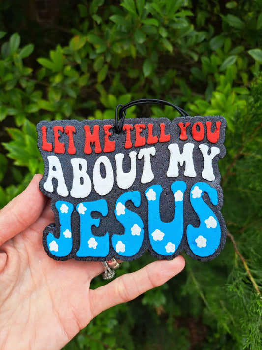 Red, white, and blue freshie that says, 'Let me tell you about my Jesus' message held against a green leafy background