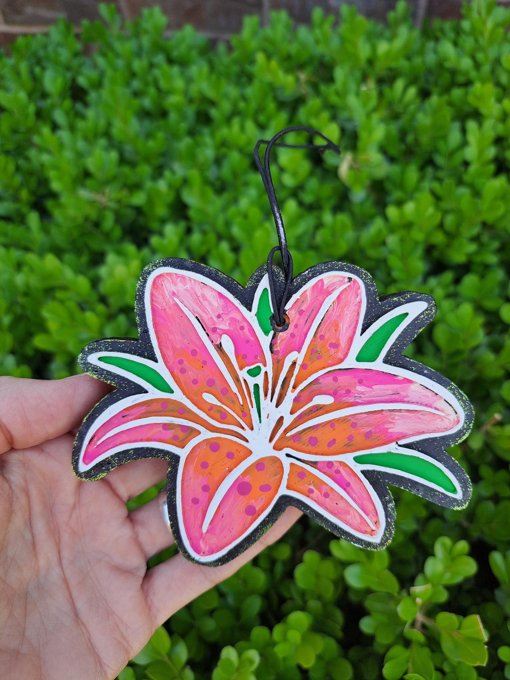 Hand holding a colorful flower-shaped air freshener against a green leafy background