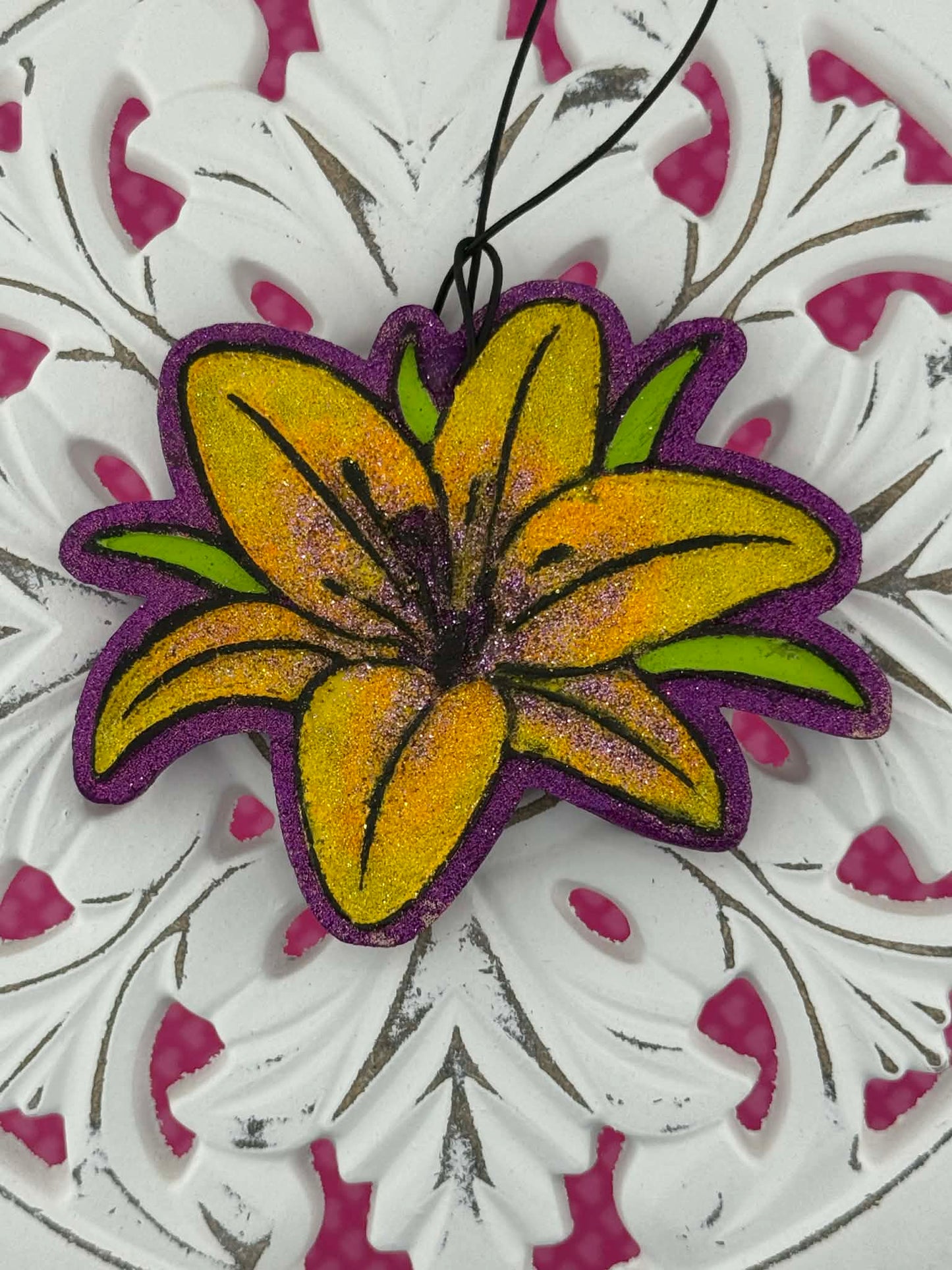 Lily shaped freshie with yellow center and purple edges on a white and pink floral background.