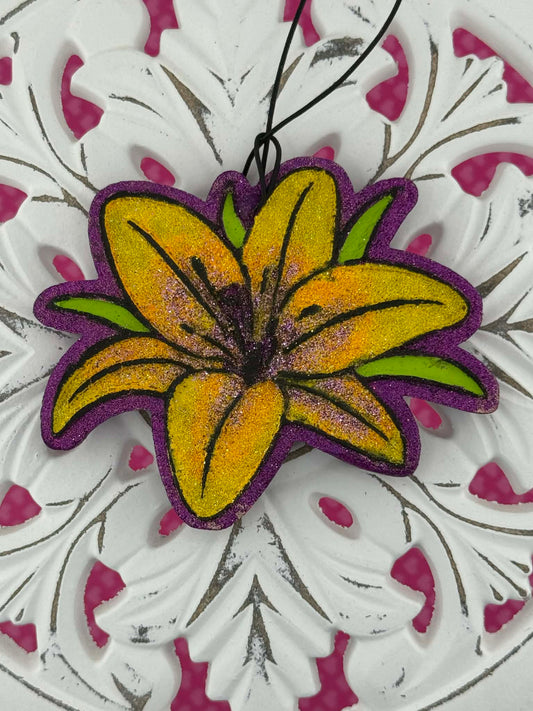 Lily shaped freshie with yellow center and purple edges on a white and pink floral background.