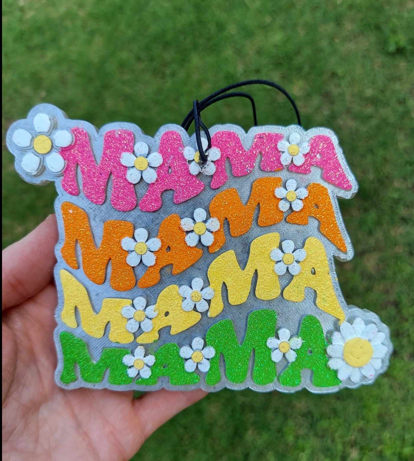 Handmade air freshener, decorated with colorful flowers and the word 'Mama' in different colors, held in a hand.