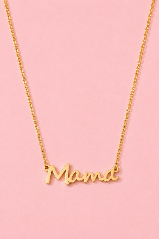 A gold script nameplate necklace spelling 'Mama' on a delicate gold chain, set against a solid light pink background.