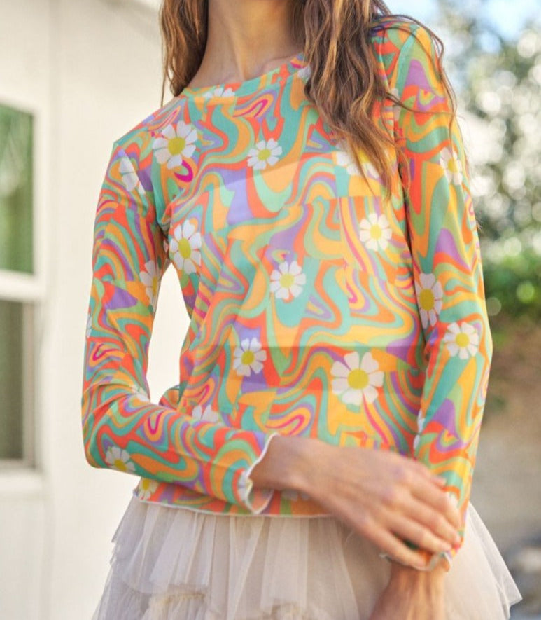 A woman wearing a multicolored floral retro print daisy mesh top with long sleeves.